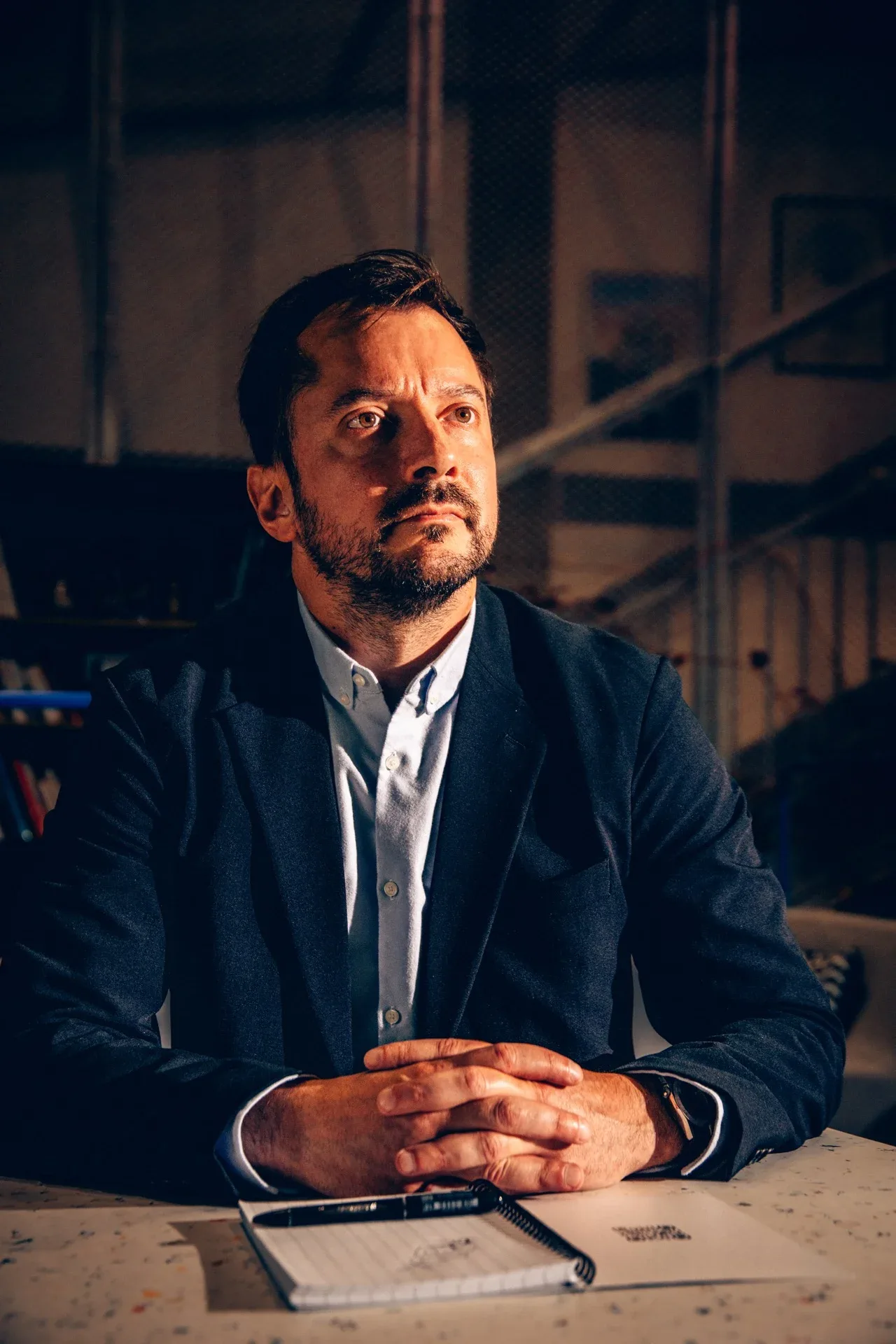 Victor Mallet, consultant en cybersécurité, assis à une table, mains jointes devant un carnet, regard au loin