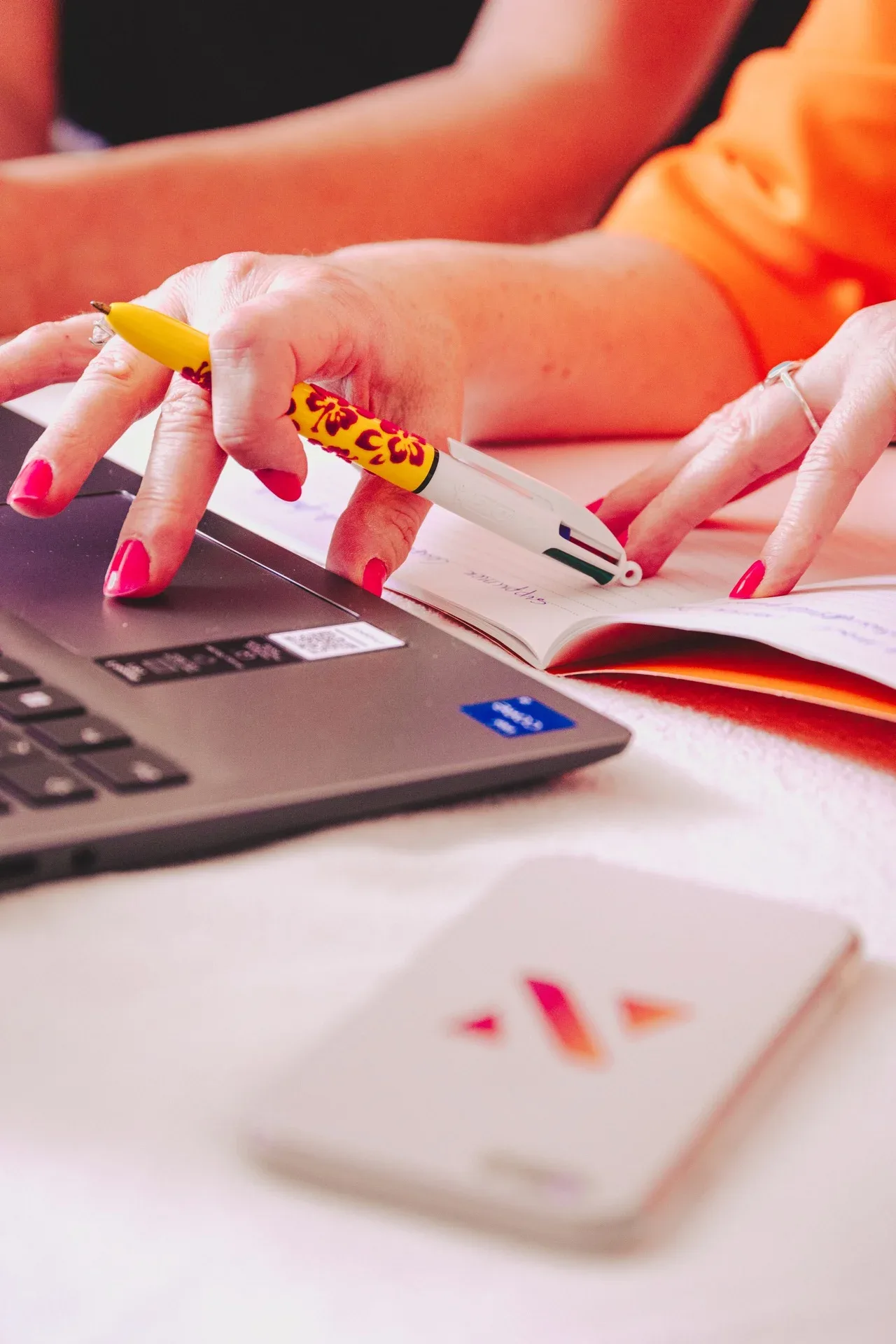 Mains de Nelly Audrain au bureau, stylo fleuri entre ordinateur portable et carnet