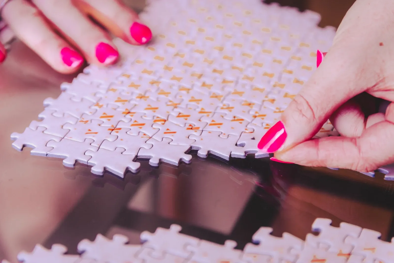 Gros plan sur les mains aux ongles roses de Nelly assemblant un puzzle