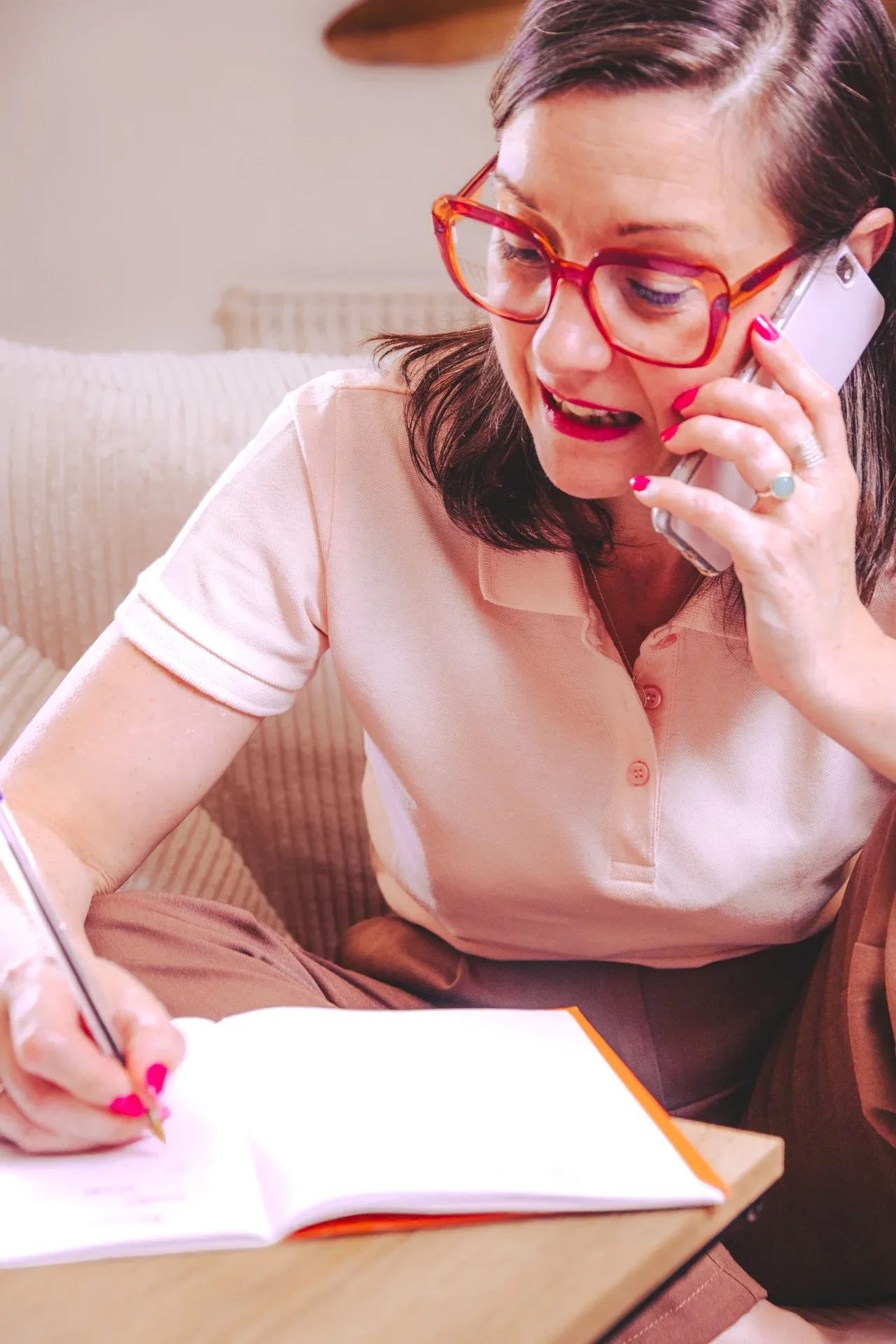 Nelly Audrain en polo rose pâle au téléphone, prenant des notes dans un carnet