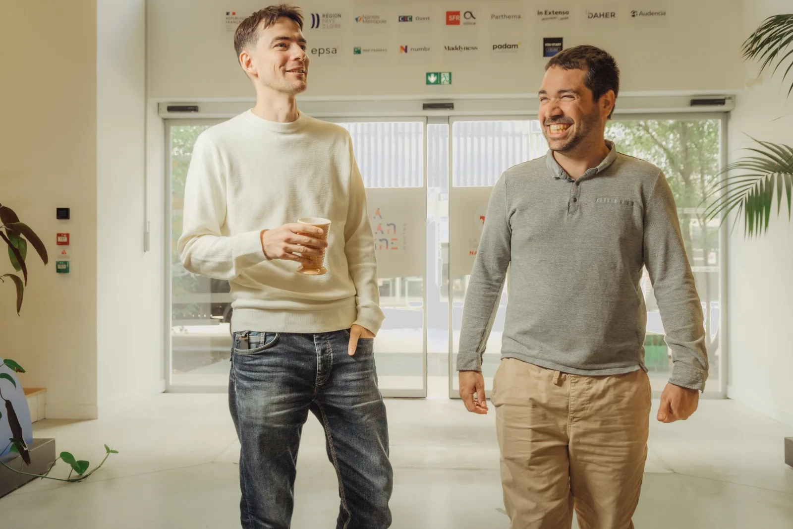 Deux associés de Lonestone riant ensemble dans un hall lumineux, café à la main