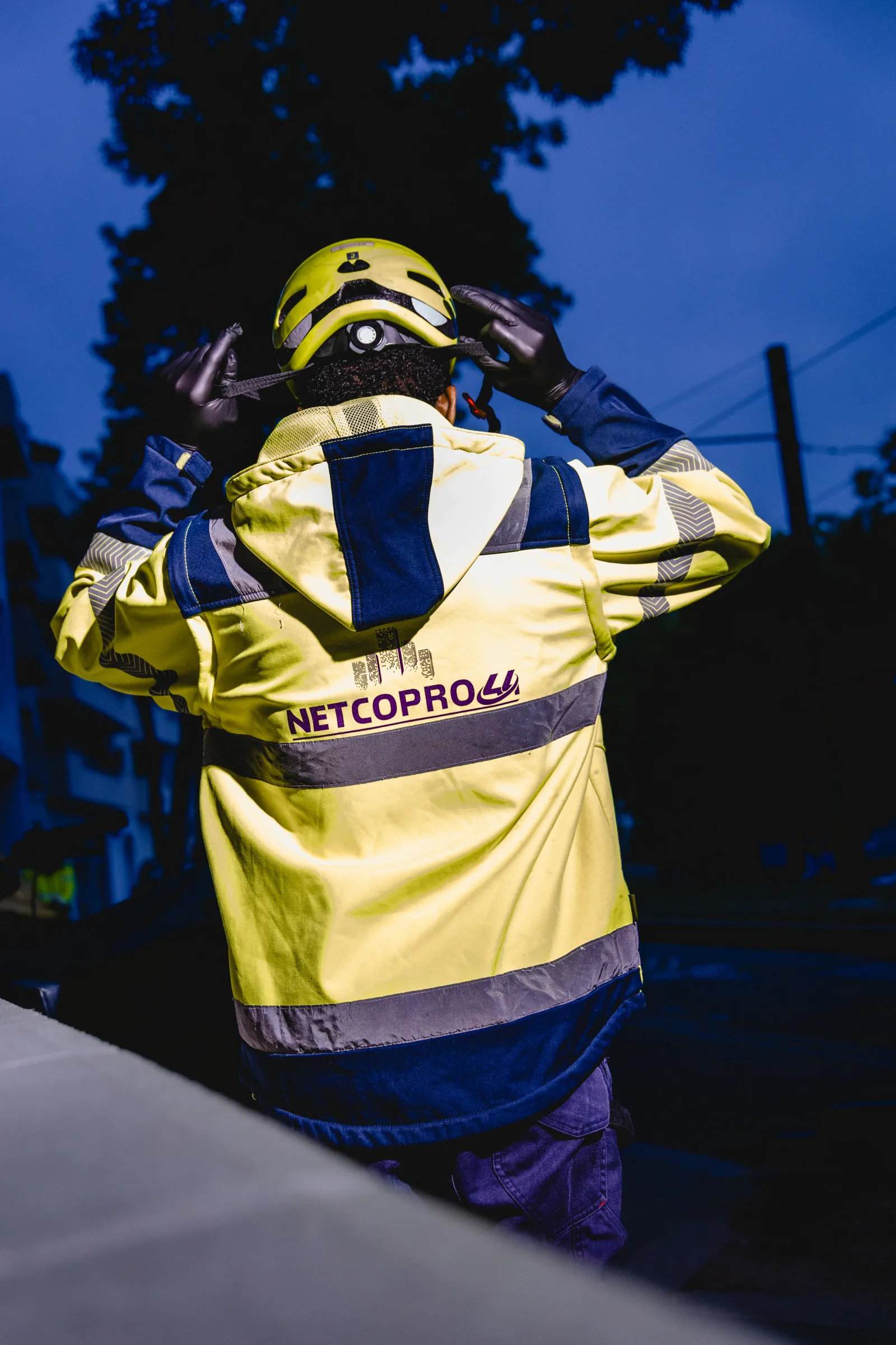 Agent Netcopro44 de dos en veste haute visibilité, ajustant son casque à l'aube
