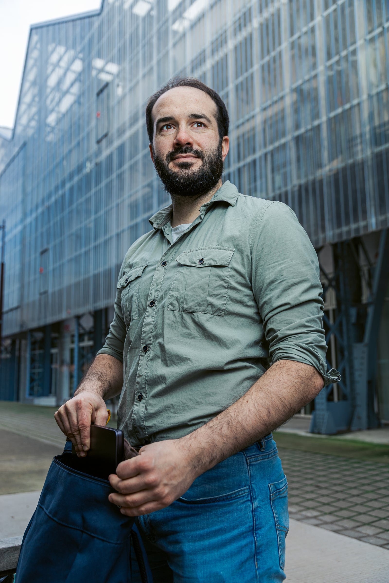 Développeur freelance glissant un appareil dans son sac devant une façade vitrée industrielle