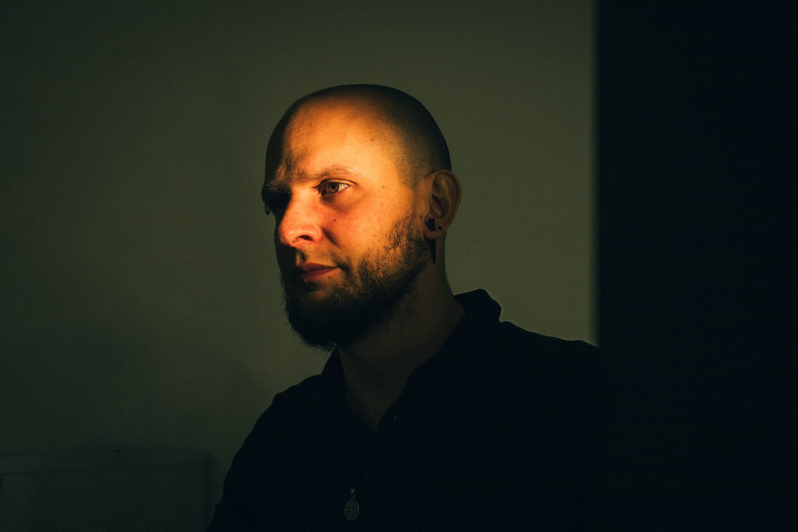 Pentester au crâne rasé en portrait serré, visage éclairé d'une lumière orangée ciblée