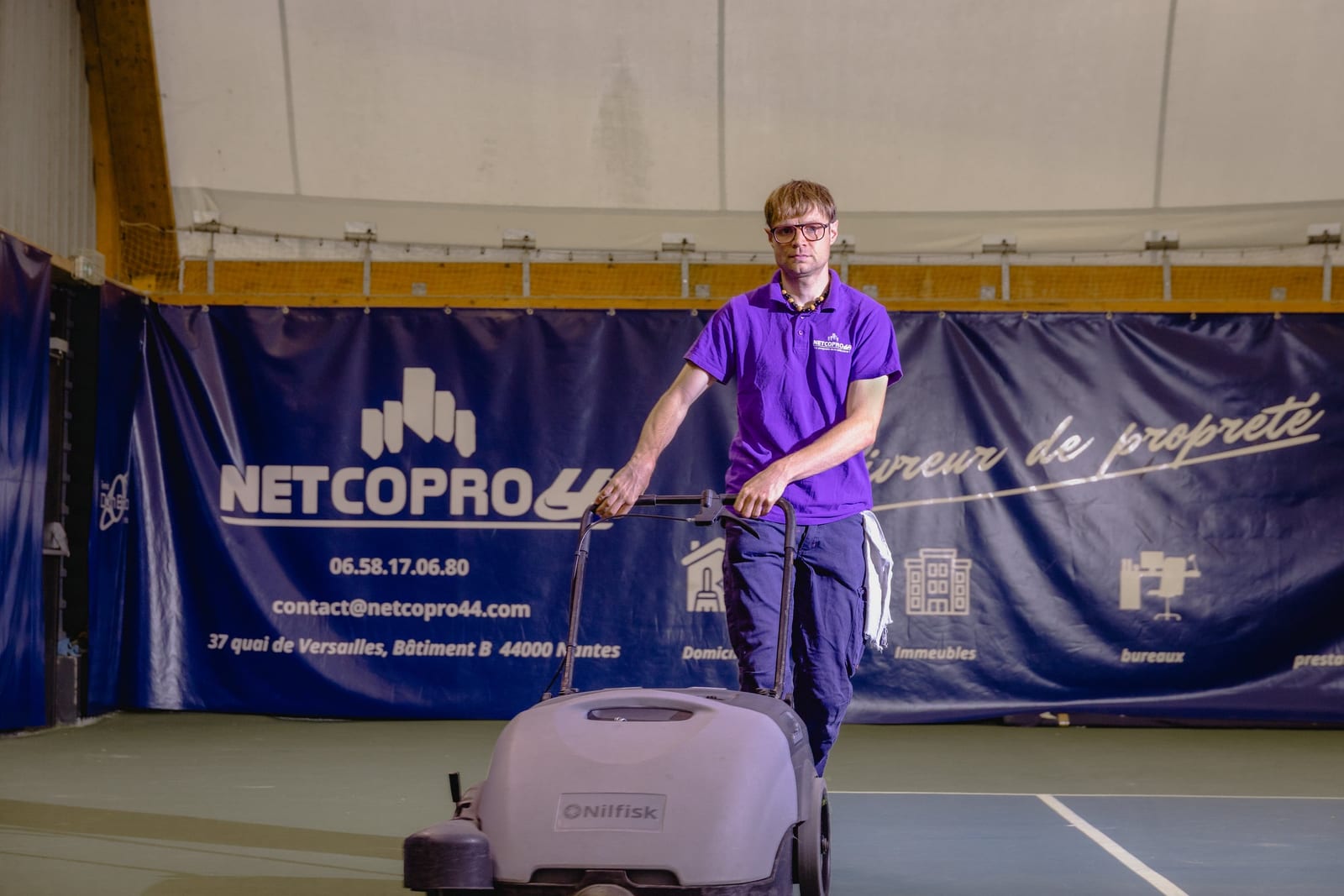Agent Netcopro44 poussant une balayeuse Nilfisk sur un court de tennis couvert